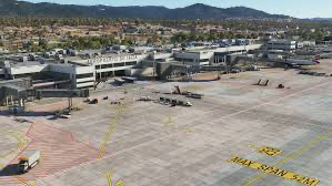 Aerial view of a large airport terminal with visible tarmac, gates, and vehicles. Helipaddy-related content.