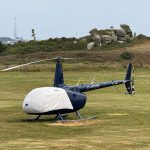 Helicopter R66 at Helipaddy landing site on grassy field with scenic background.