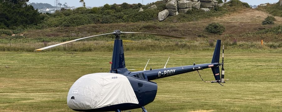 Helicopter R66 at Helipaddy landing site on grassy field with scenic background.