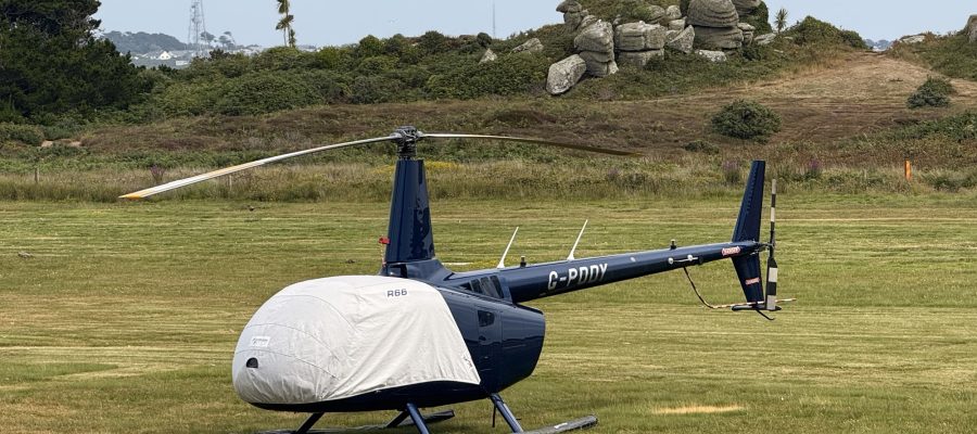 Helicopter R66 at Helipaddy landing site on grassy field with scenic background.