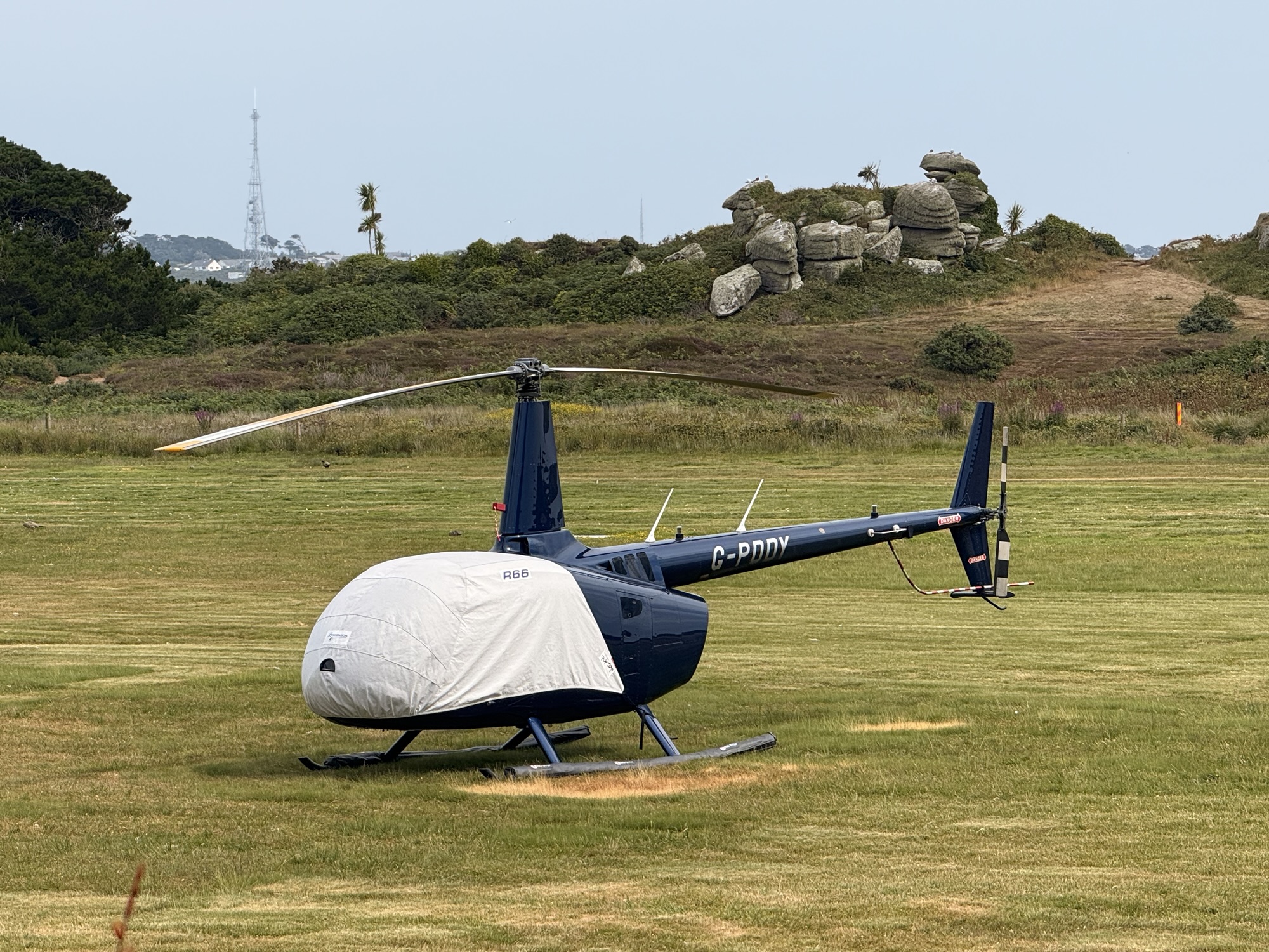 Helicopter R66 at Helipaddy landing site on grassy field with scenic background.