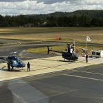 Two helicopters parked on an airfield with people nearby, highlighting Helipaddy landing locations.