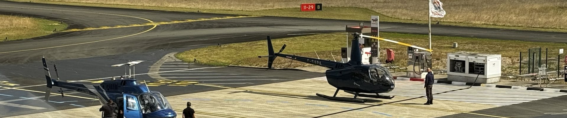 Two helicopters parked on an airfield with people nearby, highlighting Helipaddy landing locations.
