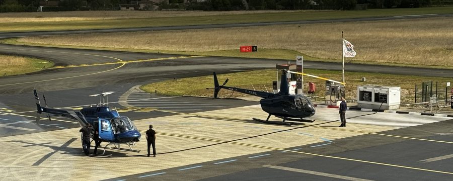 Two helicopters parked on an airfield with people nearby, highlighting Helipaddy landing locations.