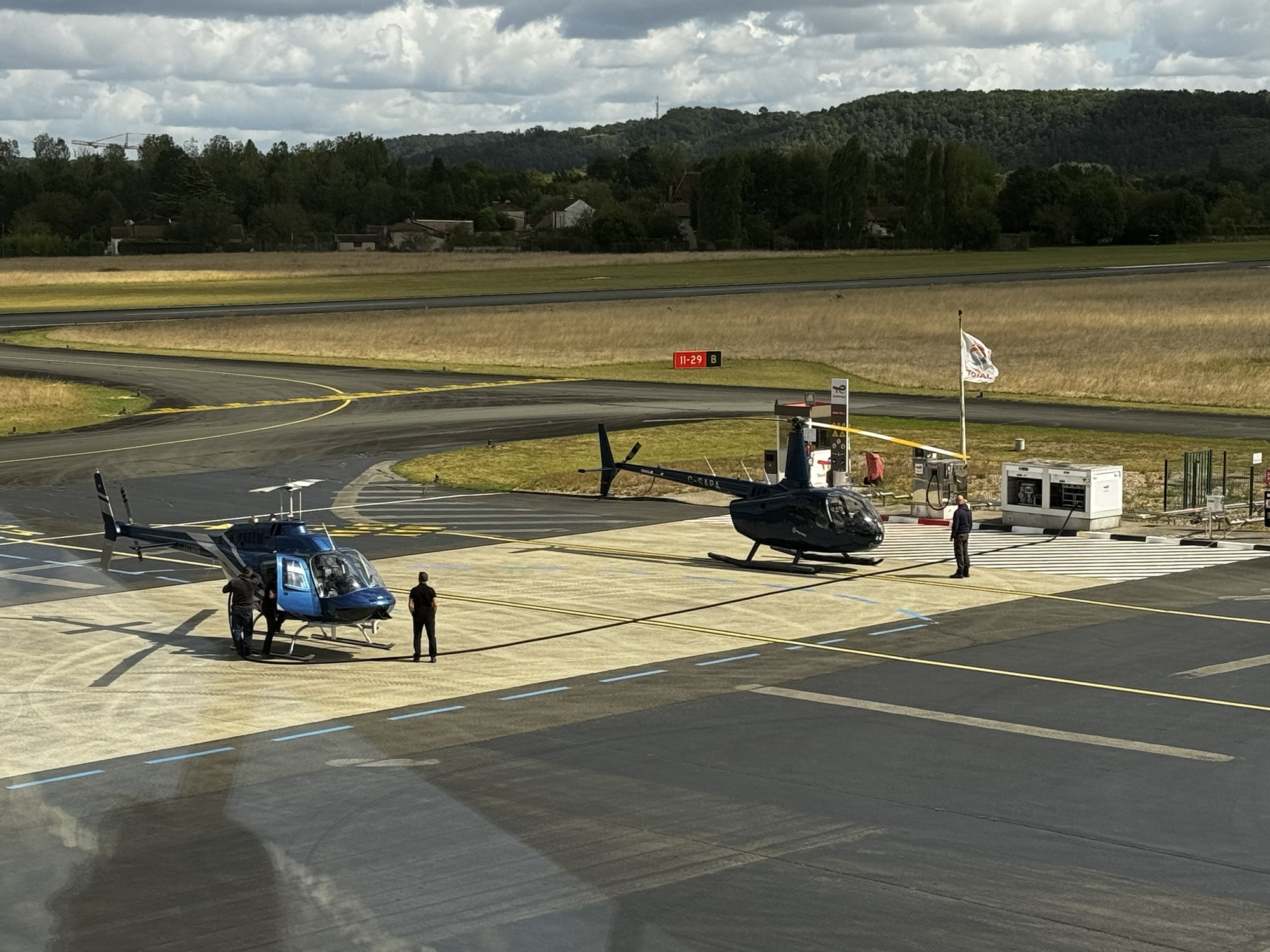 Two helicopters parked on an airfield with people nearby, highlighting Helipaddy landing locations.