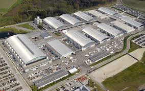 Aerial view of a large airport complex with multiple hangars and aircraft, listed on Helipaddy for pilots and travelers.