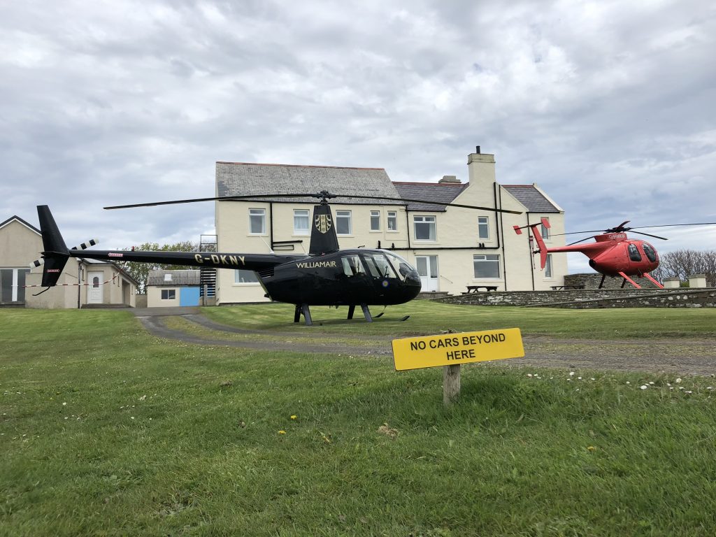 Black and red helicopters land near a building in North Scotland.